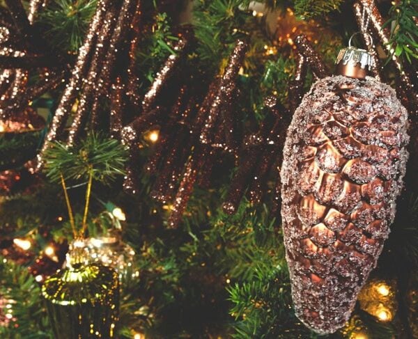 Brown-colored glittered pinecone Christmas ornament hanging on a tree branch for the perfect Christmas tree.