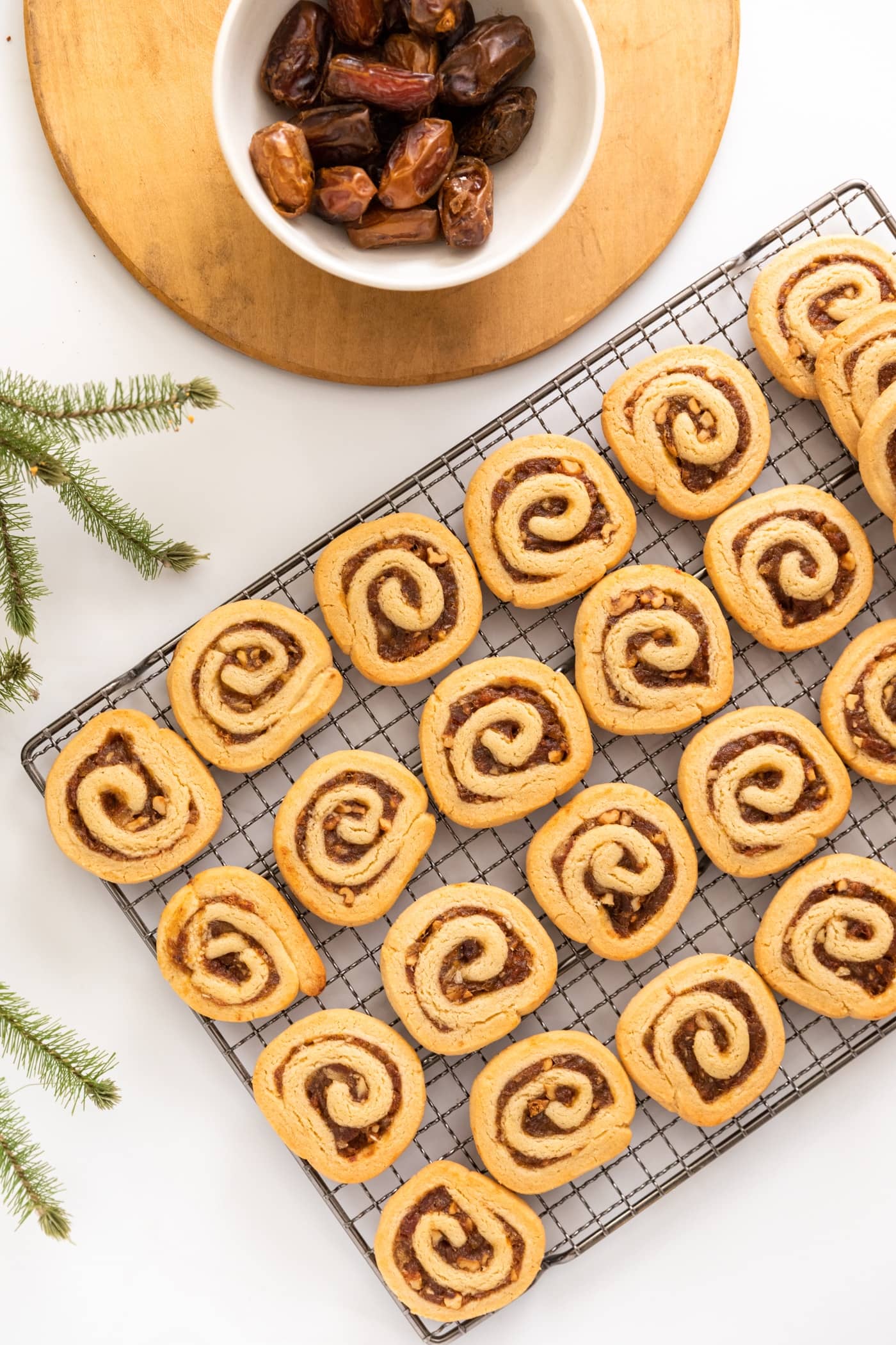 Top down view of entire rack of pinwheel cookies sitting on white surface with wood board and unpitted dates in white bowl