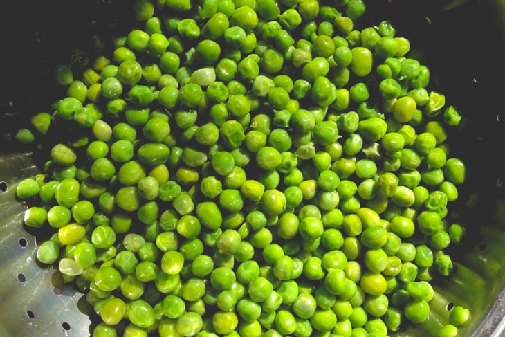 Metal strainer filled with brightly colored peas with sunlight hitting the top