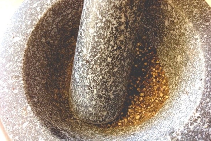Dark gray mortar and pestle with pepper being crushed in base