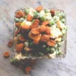 Square glass dish sitting on marble countertop filled with spring salad made from peas and eggs and topped with peanuts and cheese