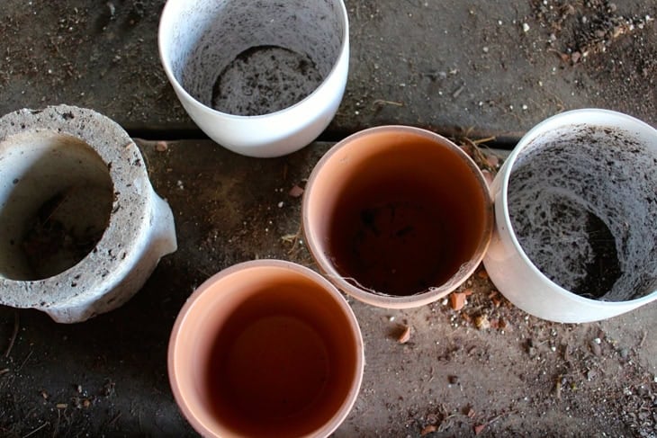 Bunch of different-looking pots sitting on a floor before being filled with soil and plants.