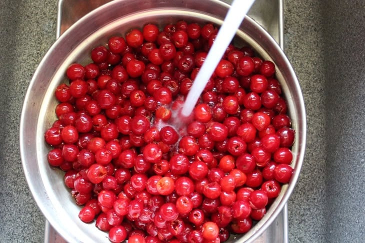 Large strainer filled with lots of pitted sour cherries with a stream of water running over the top to clean them.
