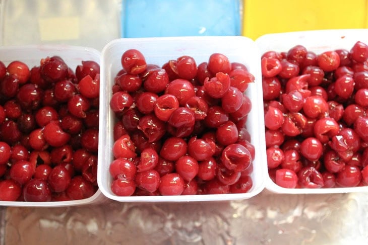 Three containers filled with sour cherries with the pits removed sitting on a countertop before putting the lids on to go into the freezer.