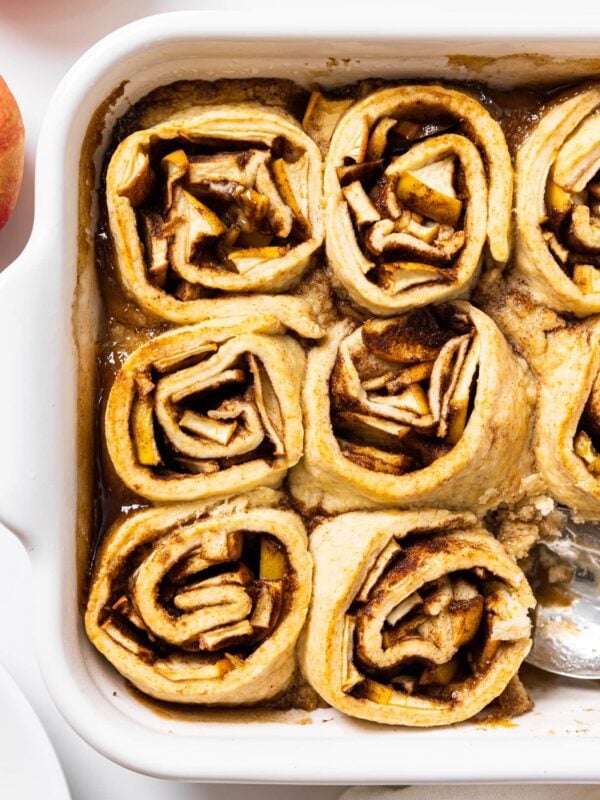 Top down view of white pan filled with rolled apple dumplings with cinnamon filling on white countertop
