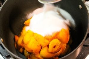 Sugar pouring on top of pile of apricots sitting in kettle on the stove