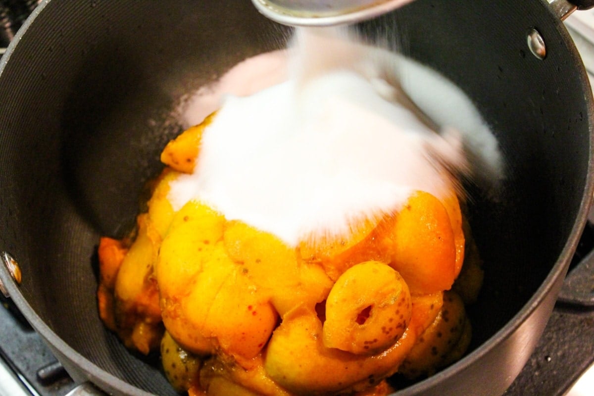 Sugar pouring on top of pile of apricots sitting in kettle on the stove