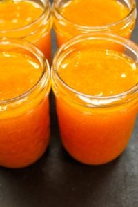 Four glass jars filled with apricot butter on a dark black surface