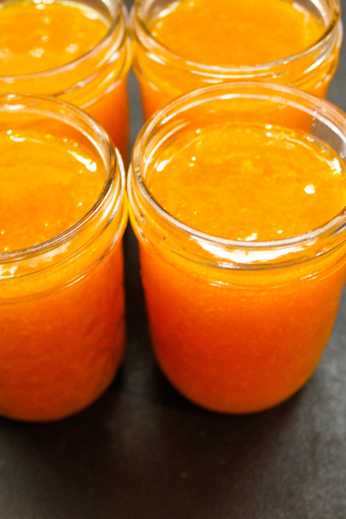 Four glass jars filled with apricot butter on a dark black surface