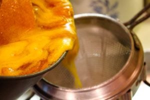 Apricot butter mixture being poured into a conical strainer set over a 9x13 pan