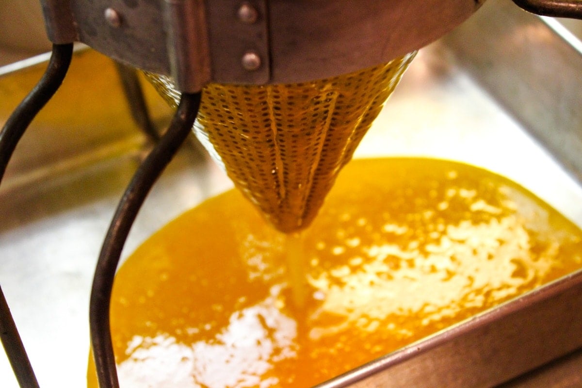 Apricot butter mixture spilling out of bottom of conical strainer into a 9x13 silver metal pan