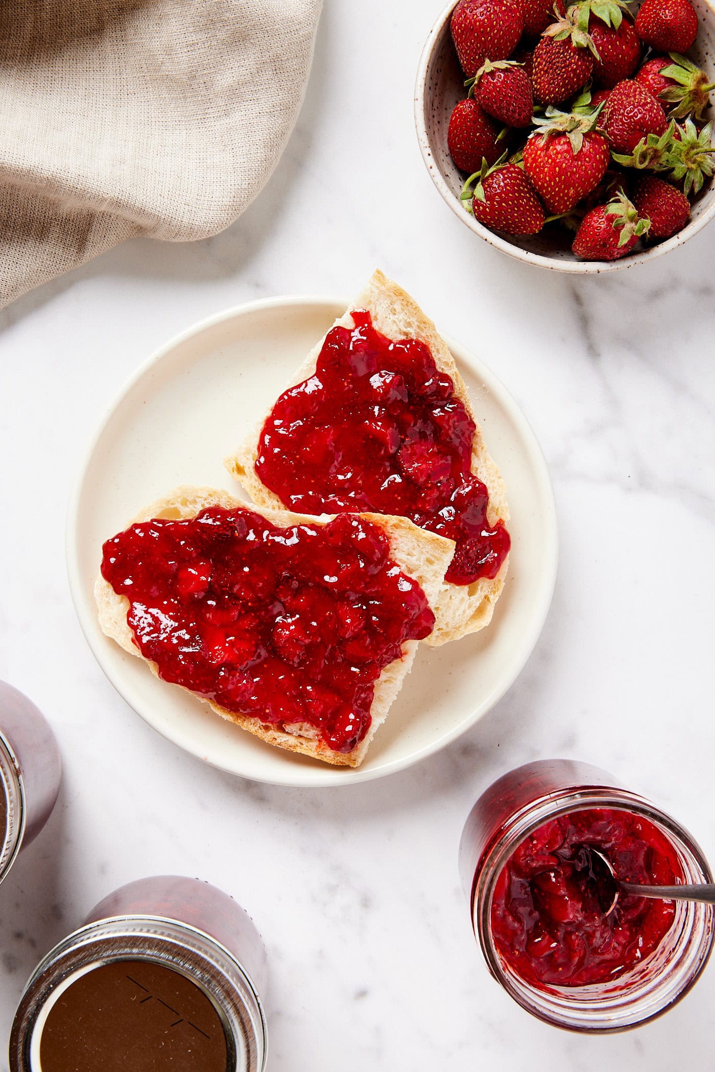White plate on white marble surface with pieces of bread with strawberry jam on top.