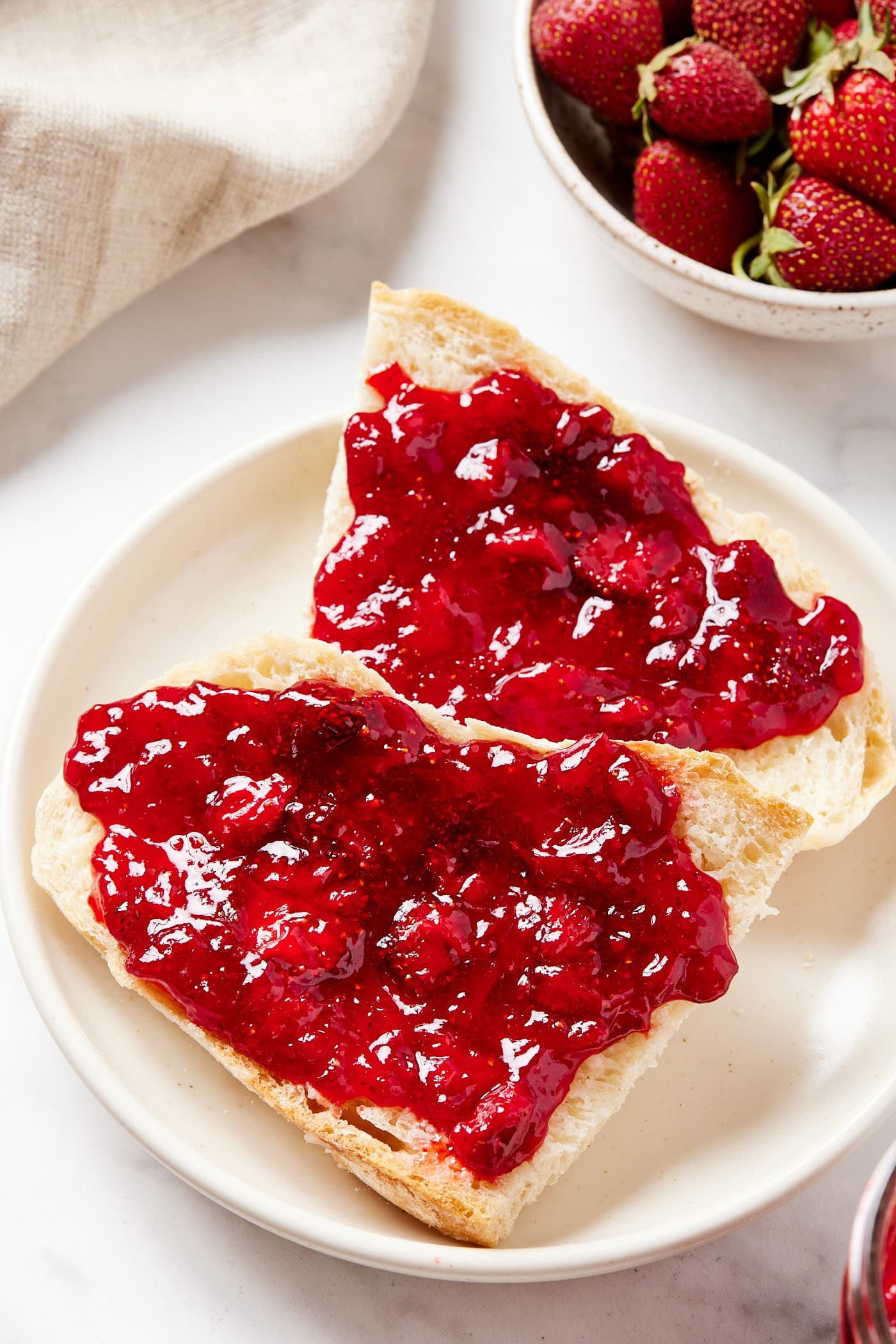 White plate with two slices of bread with jam with chunks of fruit on top.