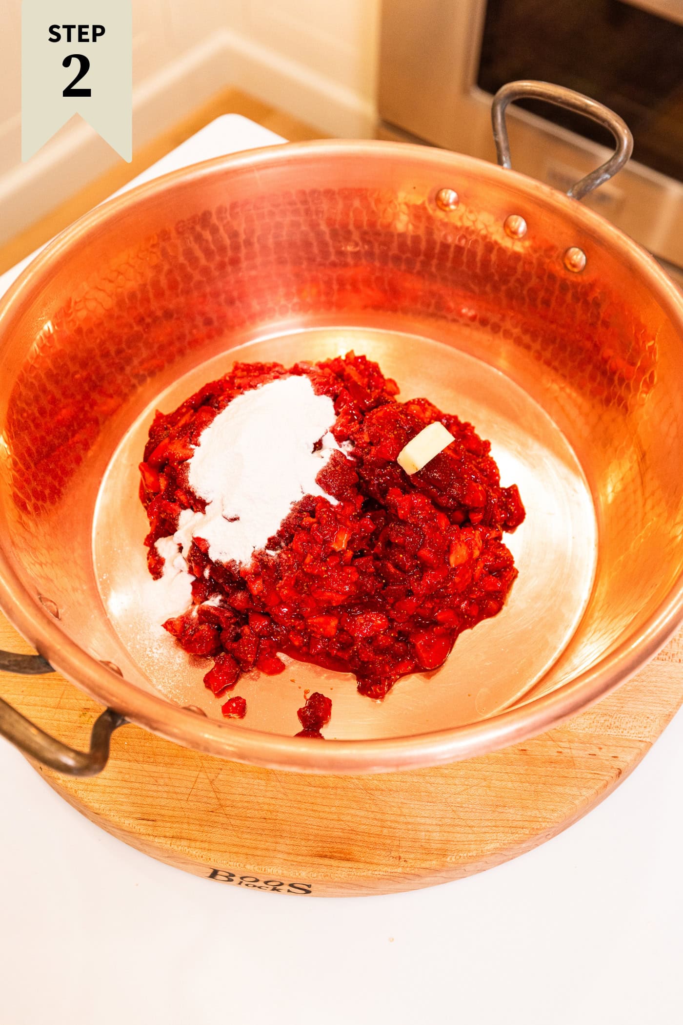 Copper pot on white surface with strawberries, pectin, and butter before being mixed together.
