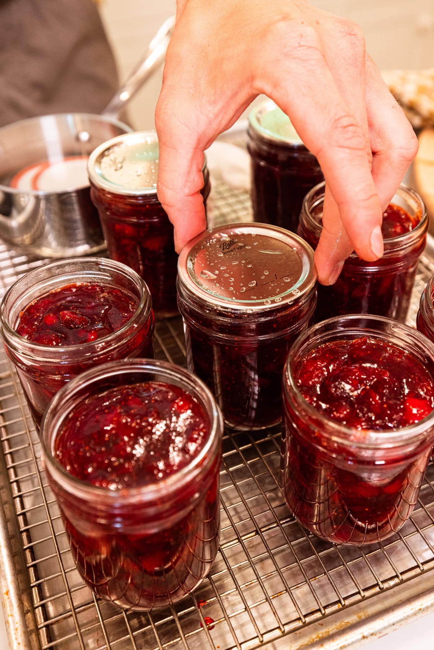 Hand holding lid on top of jam jar before canning.