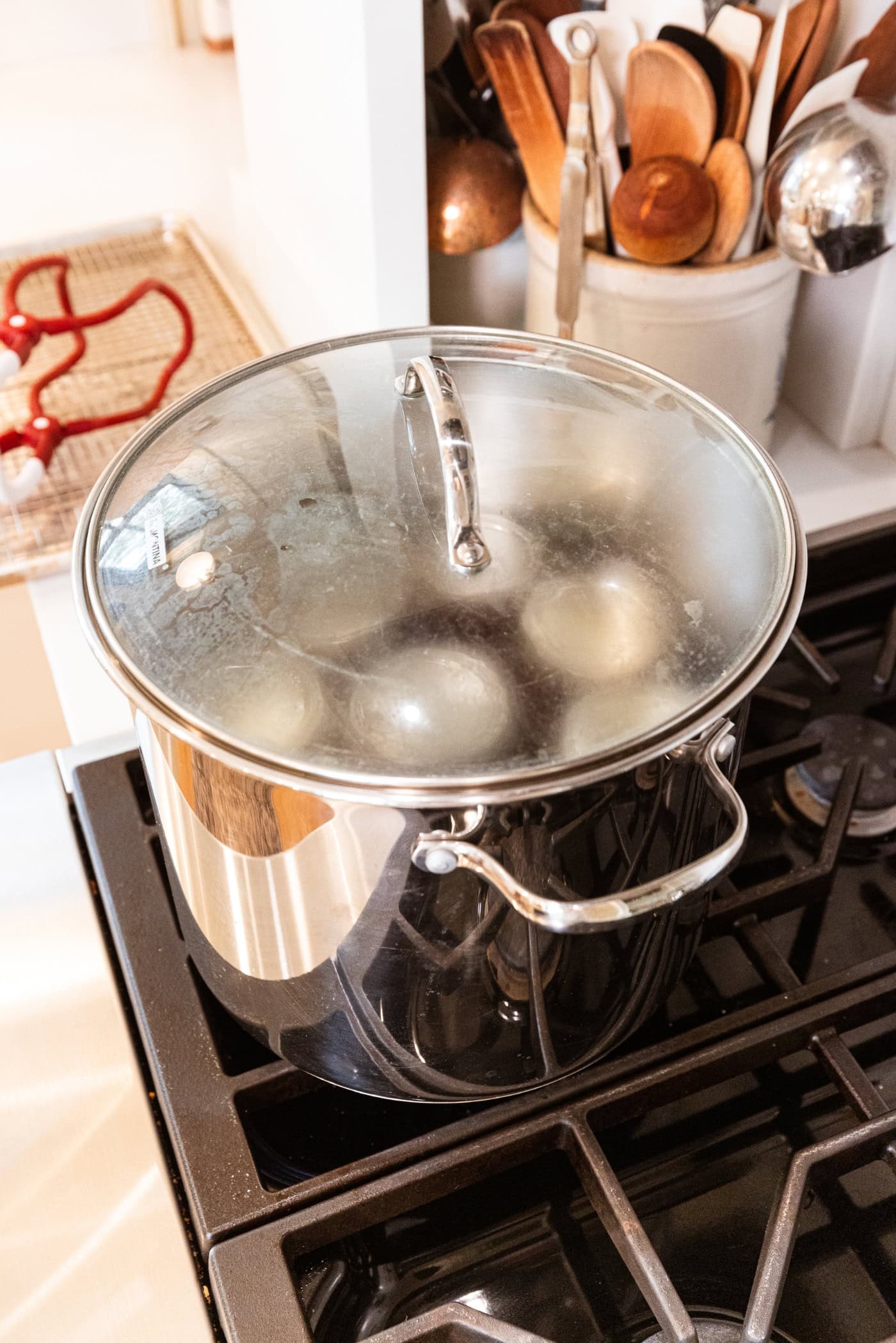 Large stockpot filled with wire rack with lid on top with jam jars filled with strawberry jam for canning.