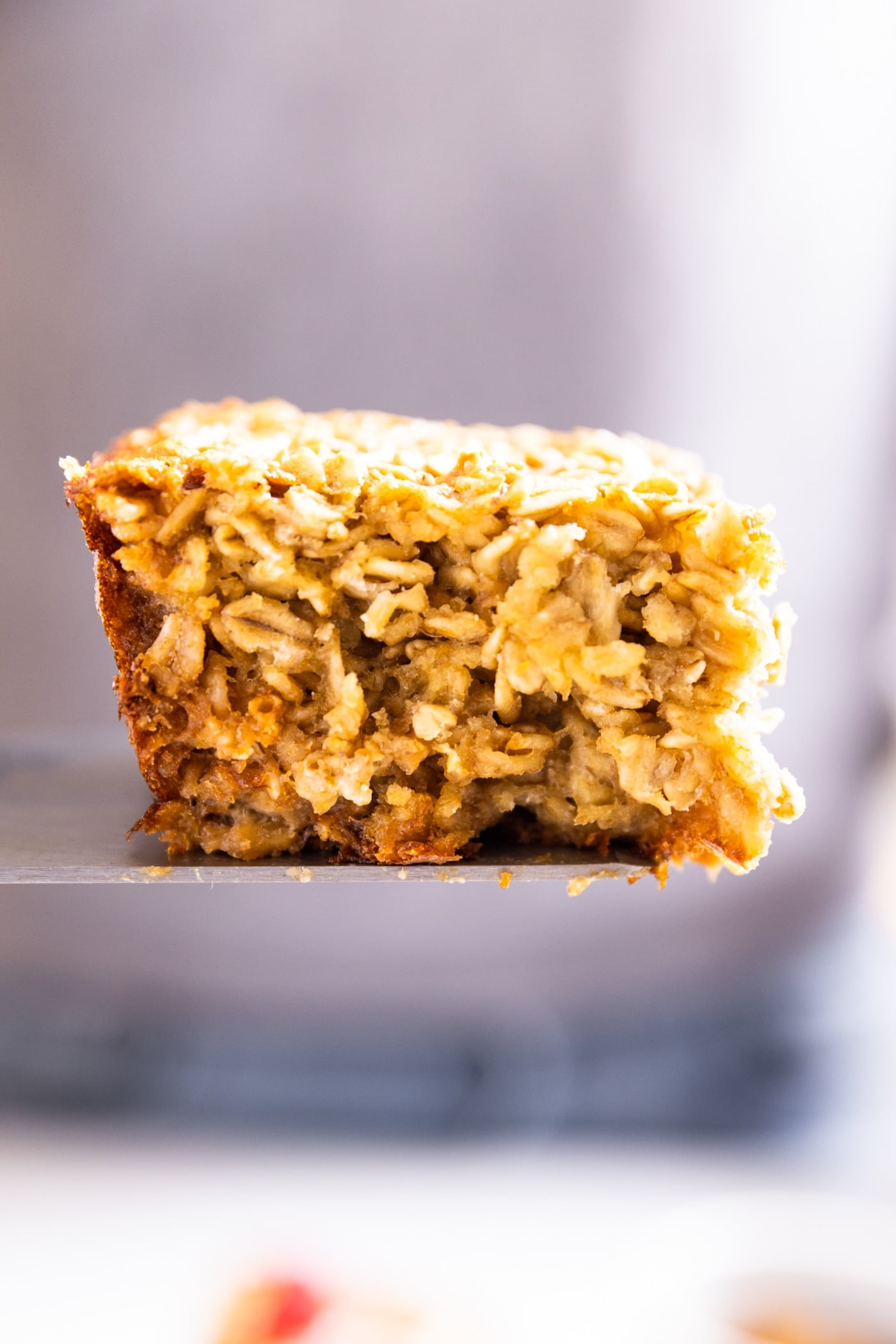 Side view of slice of baked oatmeal showing the detailed interior of a slice sitting on spatula in the air with gray shirt in background