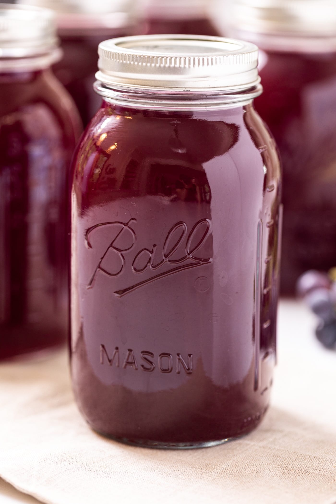 Close up view of large glass container filled with dark purple grape juice concentrate sitting on tan cloth