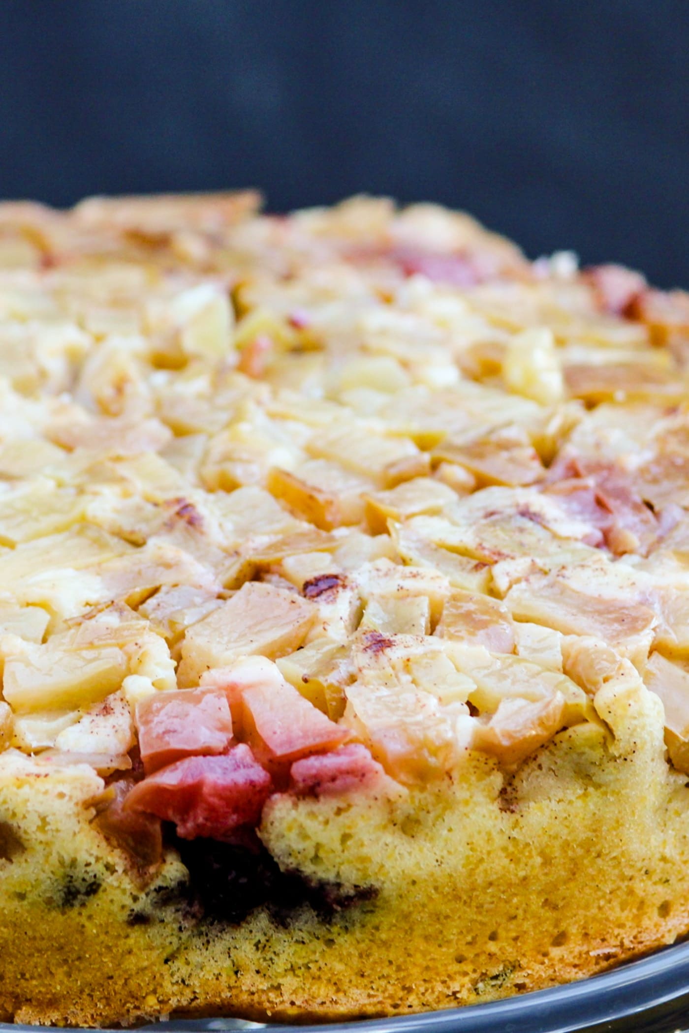 Harvest apple cake topped with apples and blackberries sitting on a cake platter with a gray slate surface