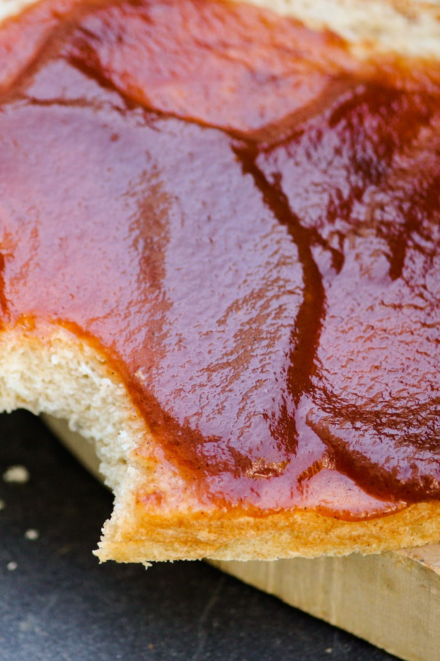 Slow cooker apple butter spread on piece of homemade bread with bite taken out on a wood cutting board on a gray slate surface