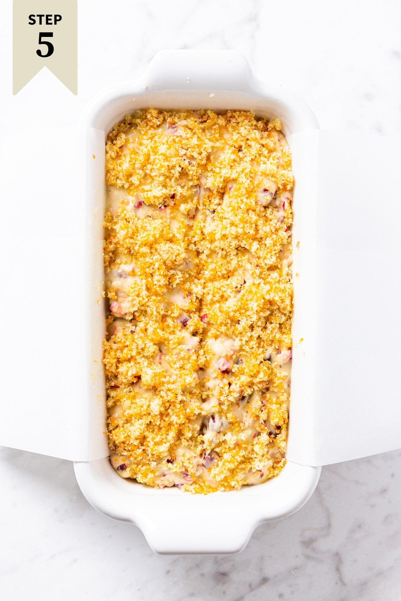White rectangular loaf pan filled with unbaked cranberry orange bread batter sitting on marble surface.
