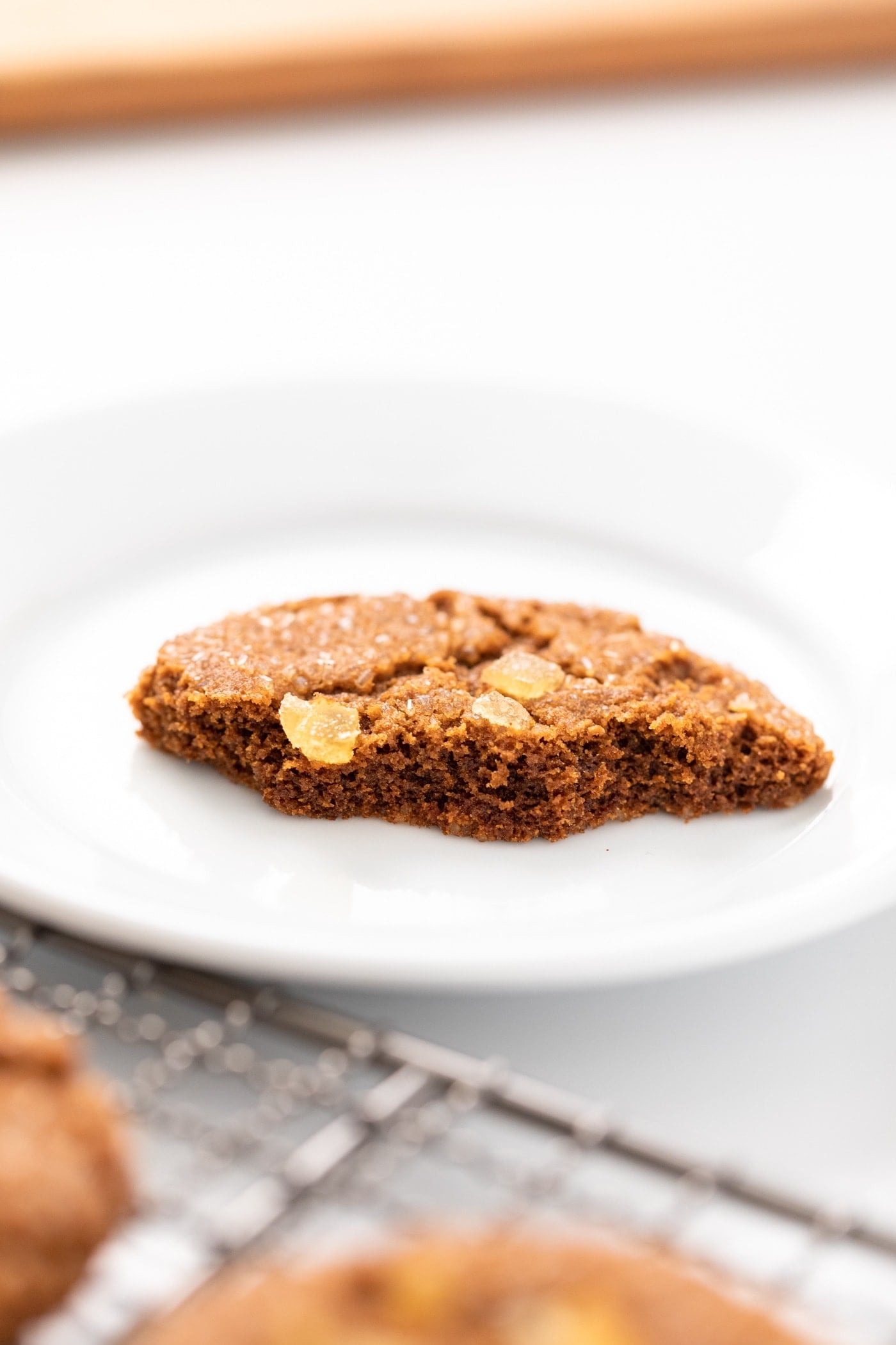 Half-eaten cookie sitting on white plate with other cookies sitting on cooling rack all on white surface
