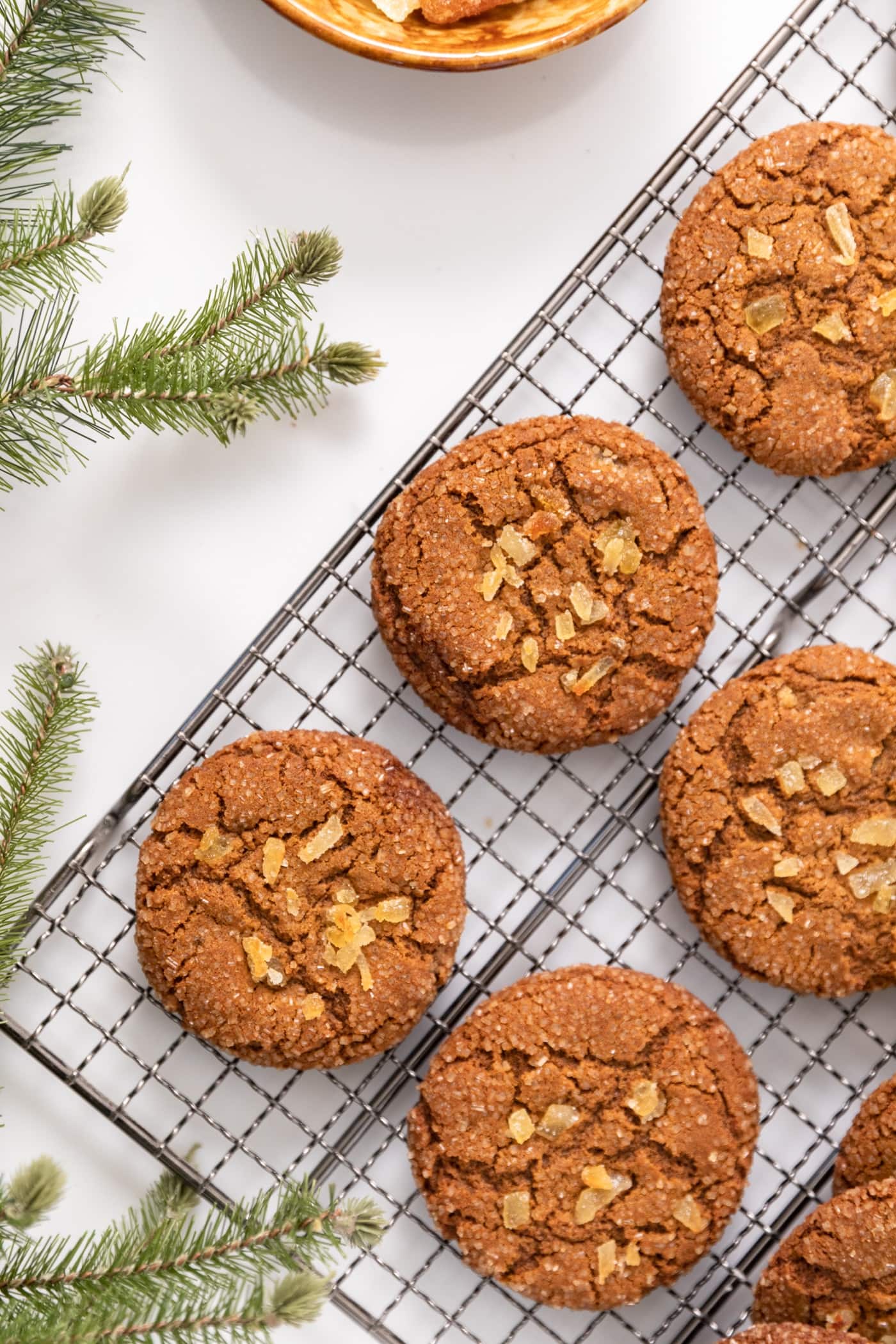 Top down view of molasses crinkle cookies sitting on cooling rack with sprigs of greens sitting around