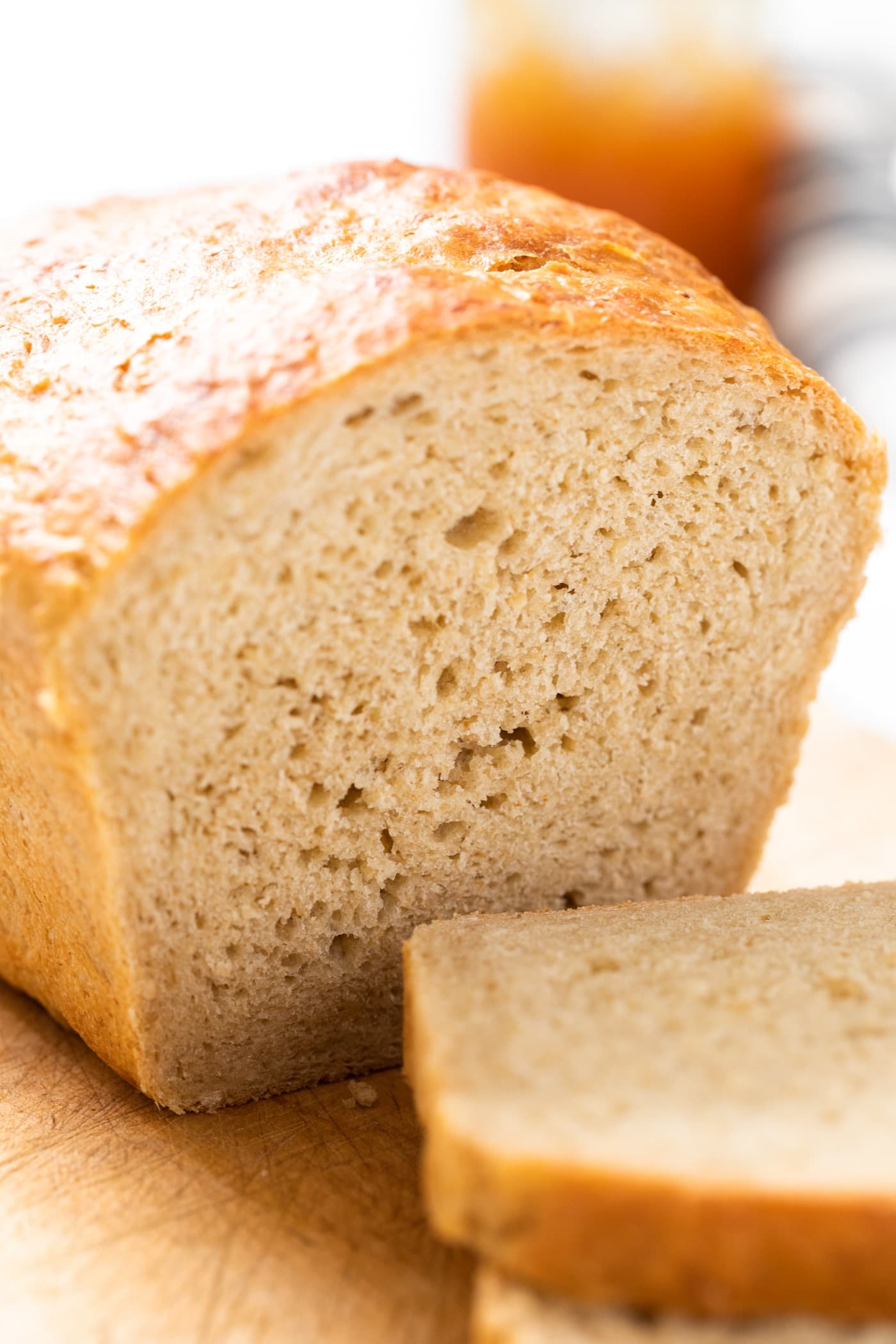 Close up view of inside of sliced bread sitting on cutting board with jam jar in background