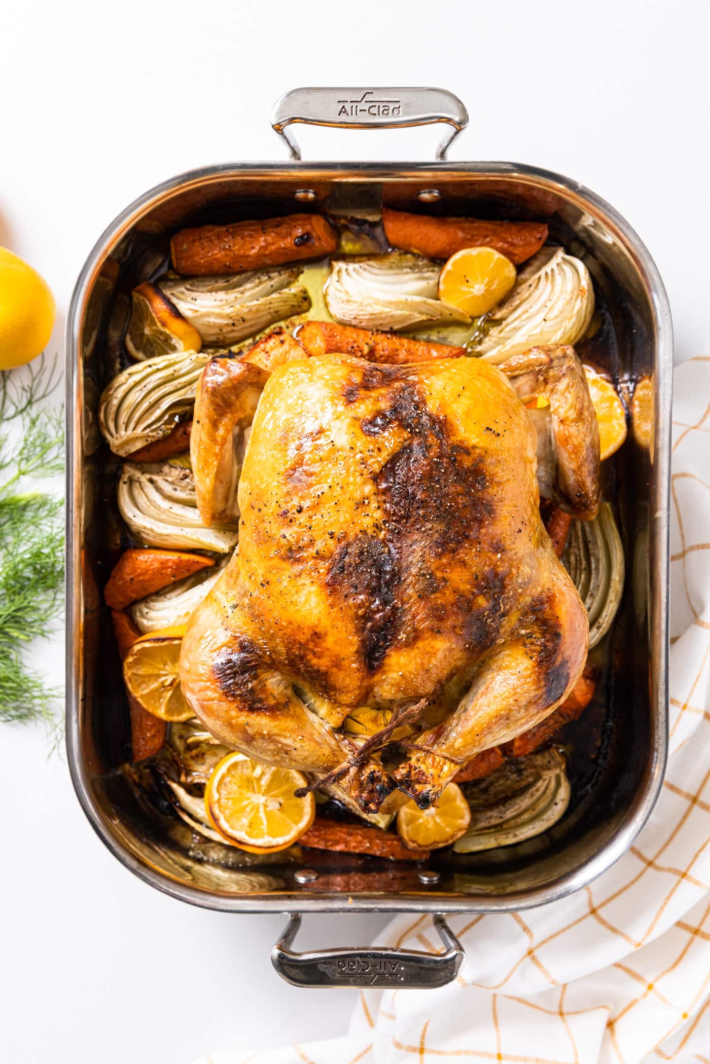 Top down view of large metal baking dish filled with roast chicken sitting on top of vegetables all on white countertop