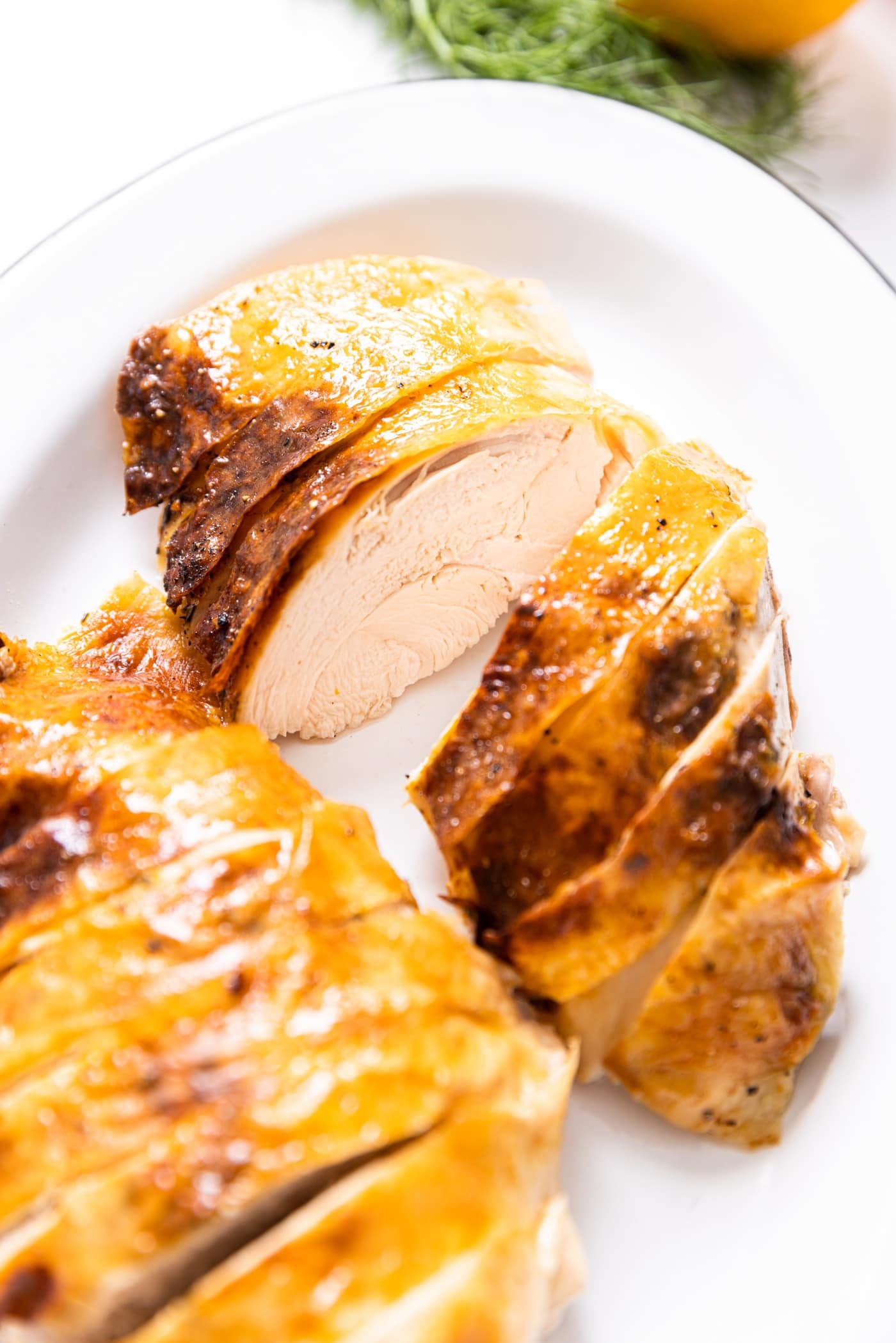 White enamel plate filled with slices of roast chicken breast with skin still on top