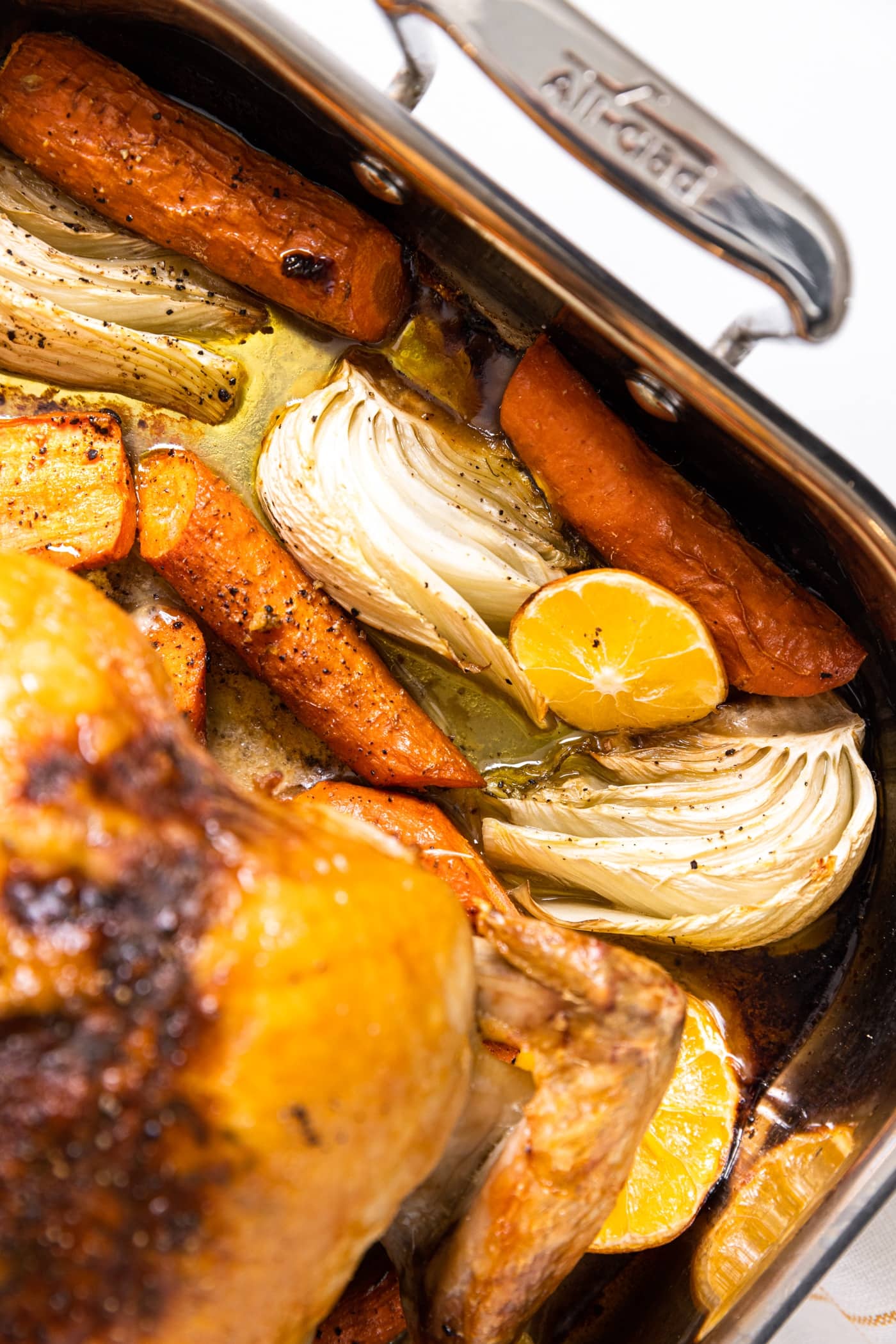 Top down view of baking dish sitting on white countertop with roasted vegetables sitting in oil after being in the oven