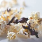 Kernels of popcorn sitting on white surface covered with chocolate