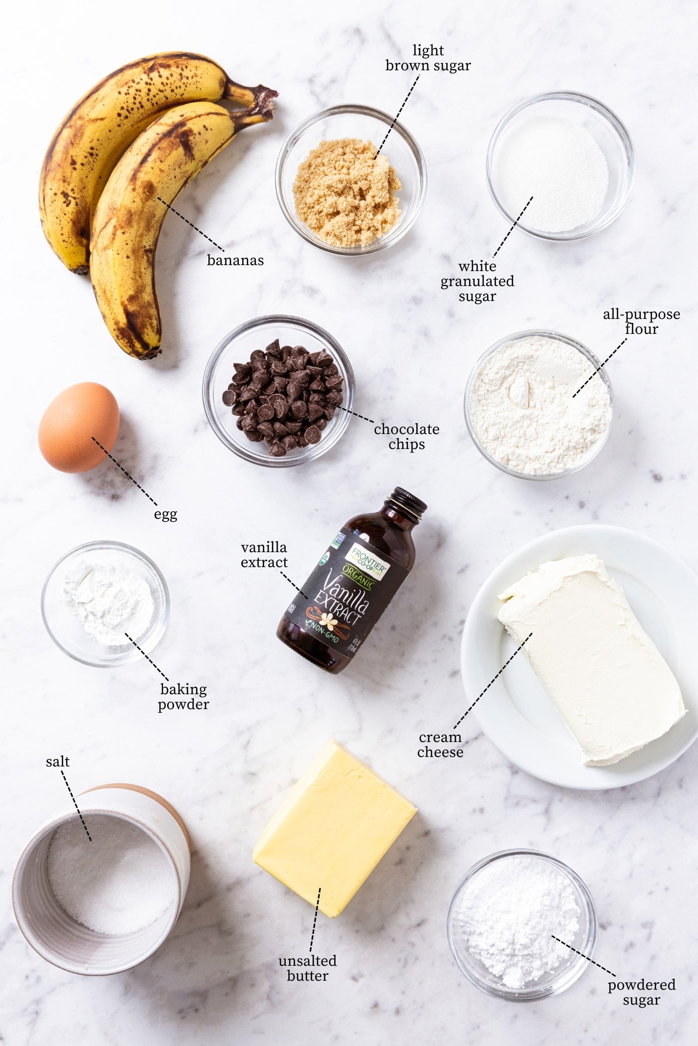 White marble surface filled with all ingredients needed to make banana bars including vanilla extract, bananas, brown sugar, white sugar, butter, egg, and more.