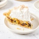 White plate sitting on a marble surface with slice of raisin pie with meringue topping.