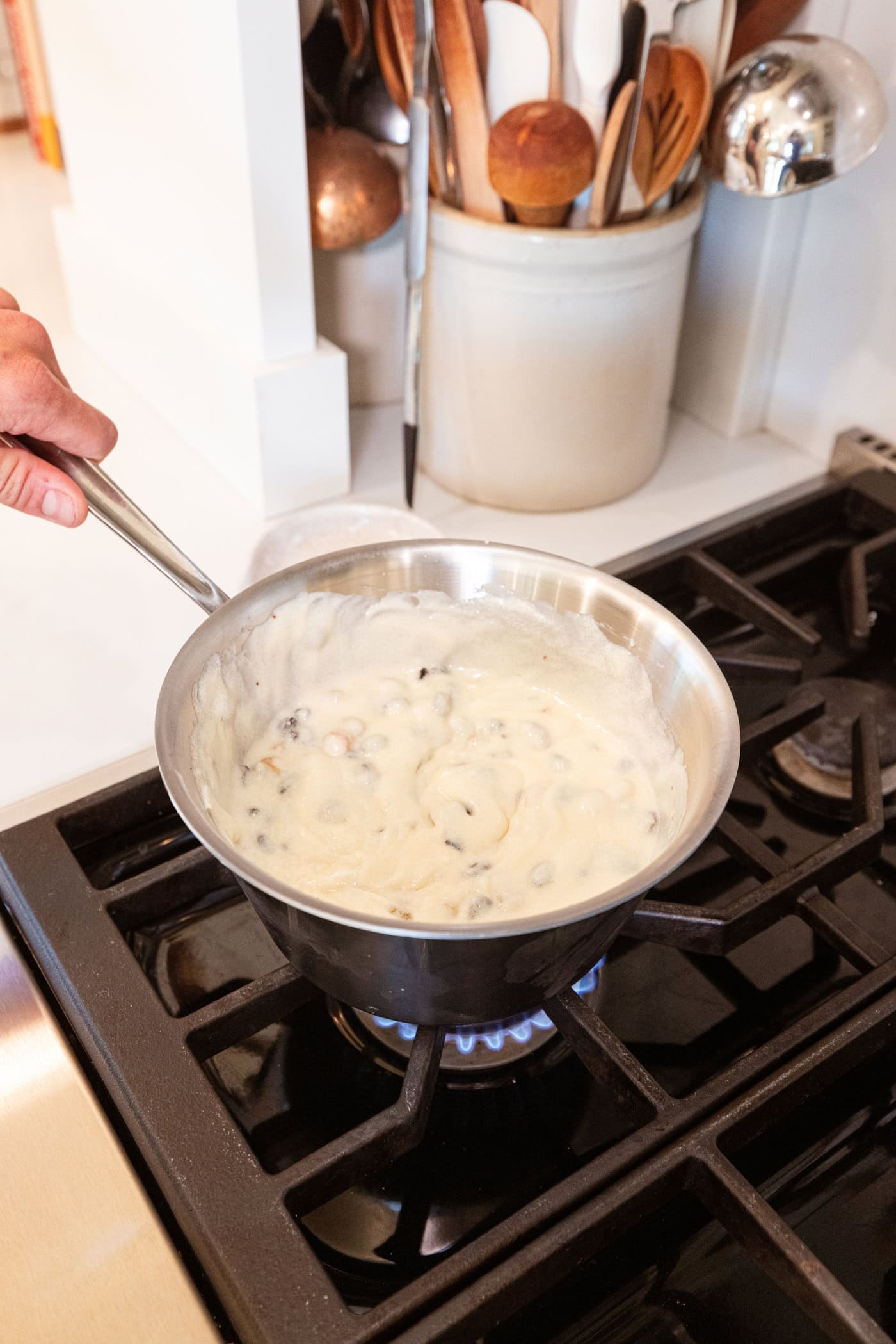 Metal saucepan on the stovetop with white-colored raisin pie filling being heated.
