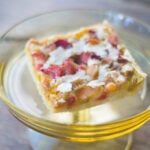 Yellow plate sitting on wood surface with square rhubarb bar sitting on plate showing red rhubarb pieces