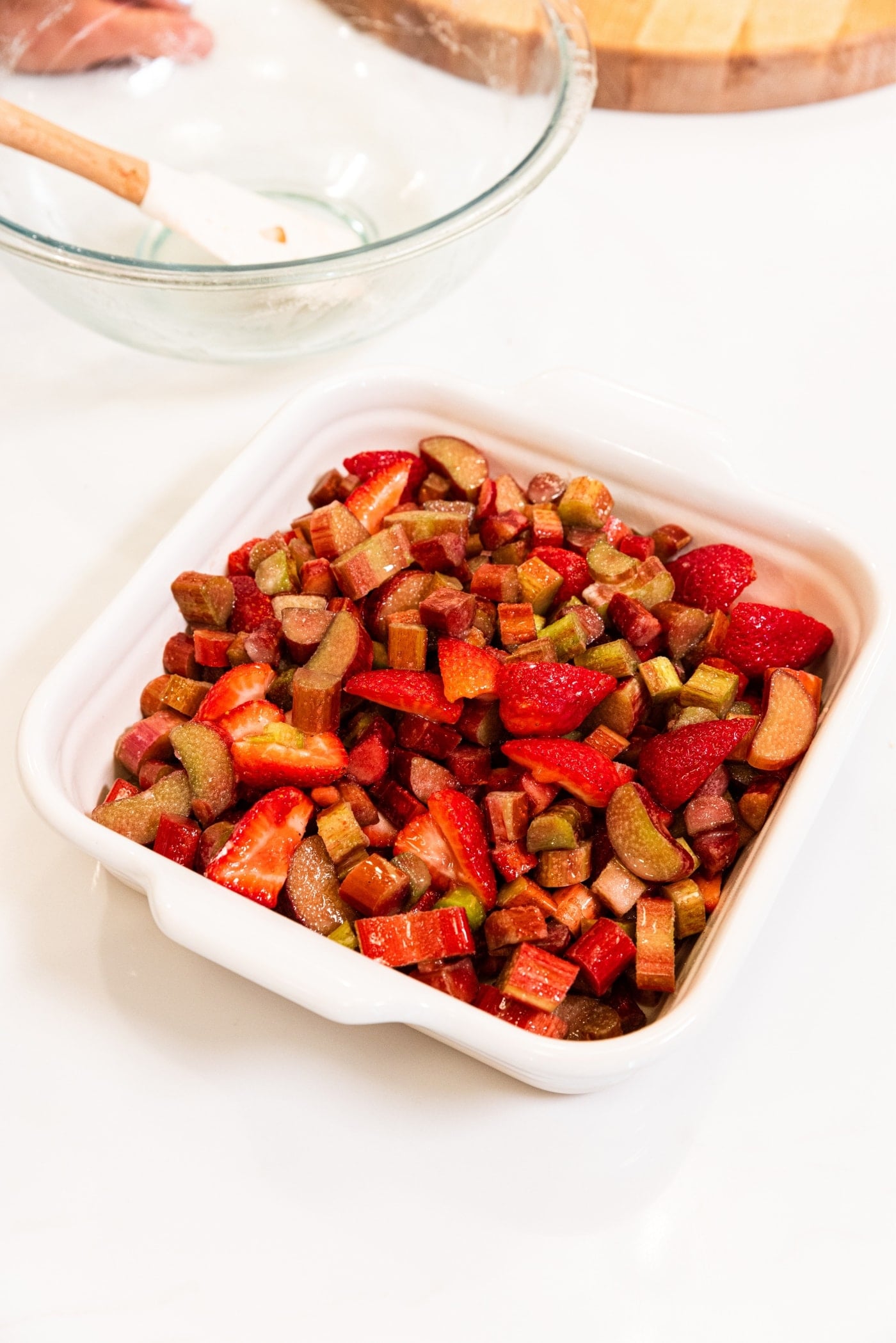 White baking dish filled with combination of chopped rhubarb and strawberries sitting on white surface.