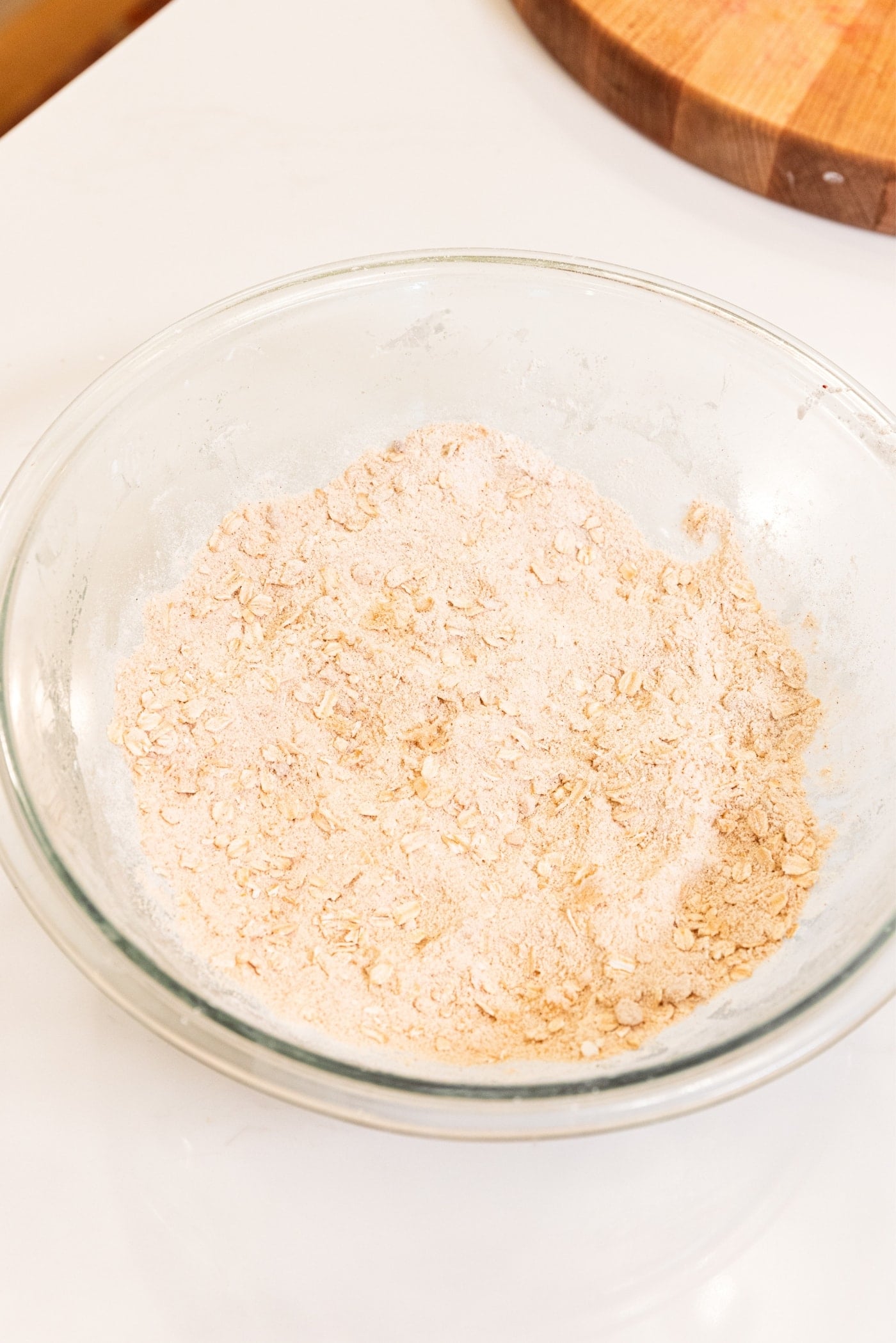 Glass bowl filled with mixture of flour and oats sitting on white surface.