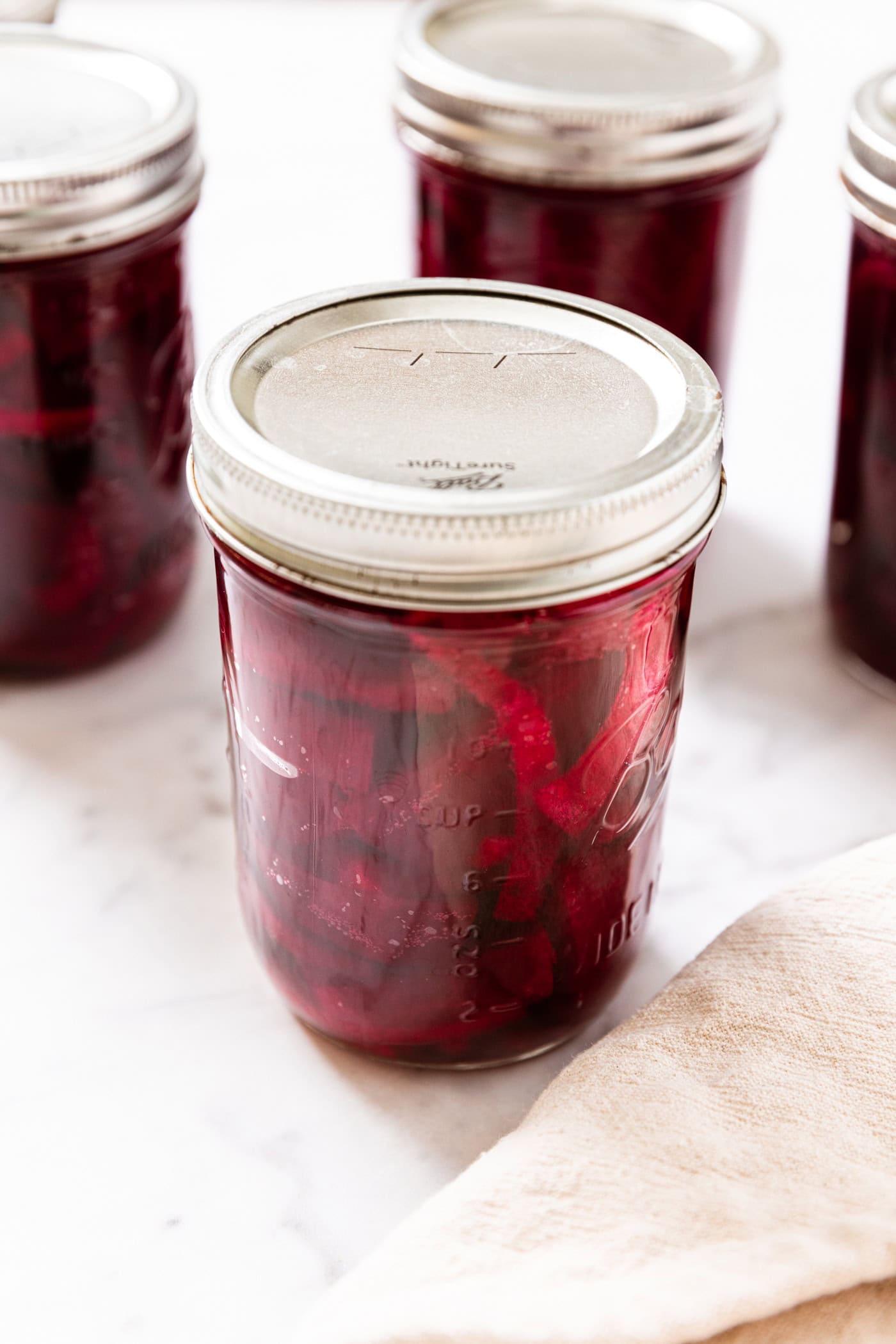 Jar filled with beets with lid and ring on top with more jars all around.