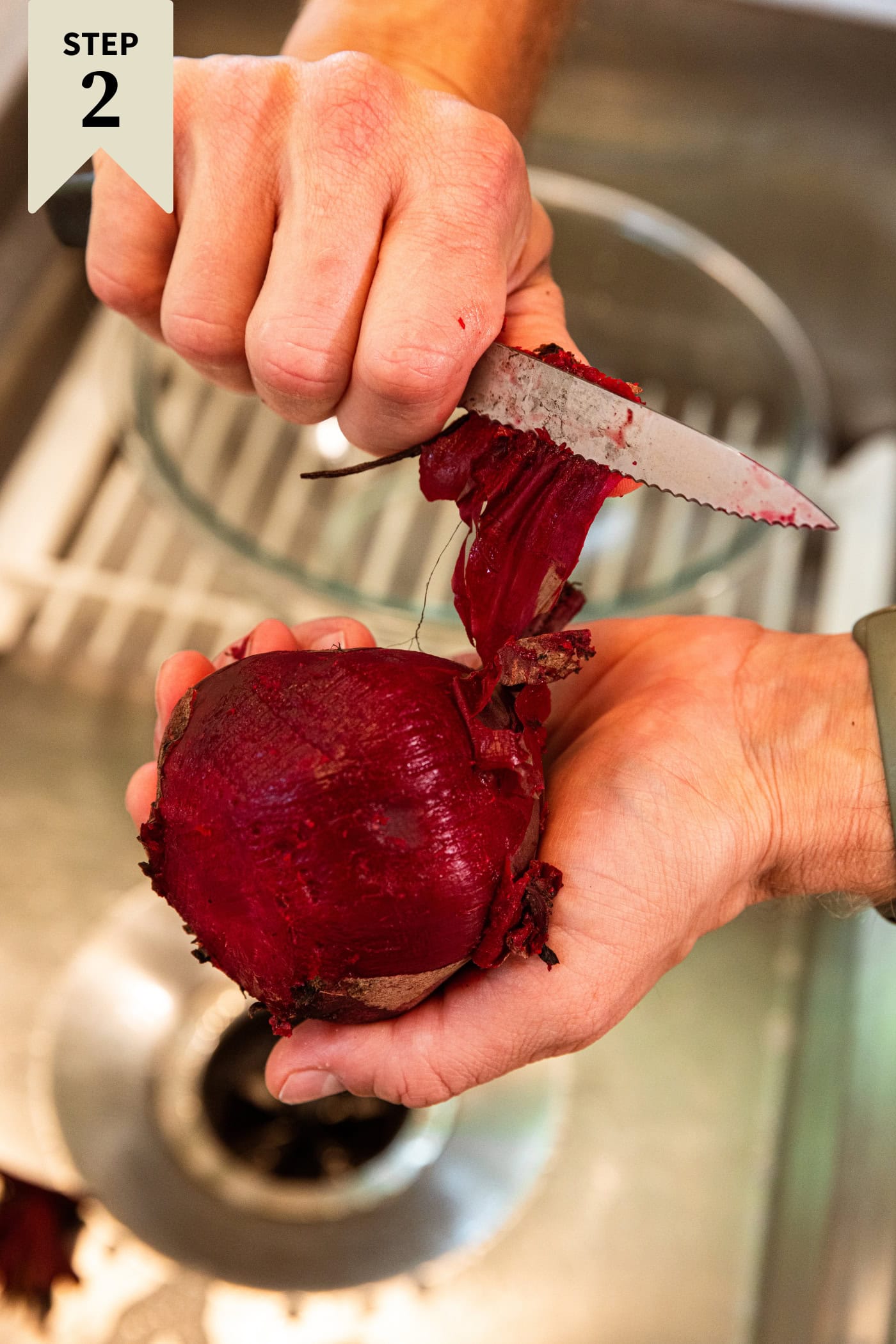 Hands holding a cooked beet peeling off the skin with the back of a knife.