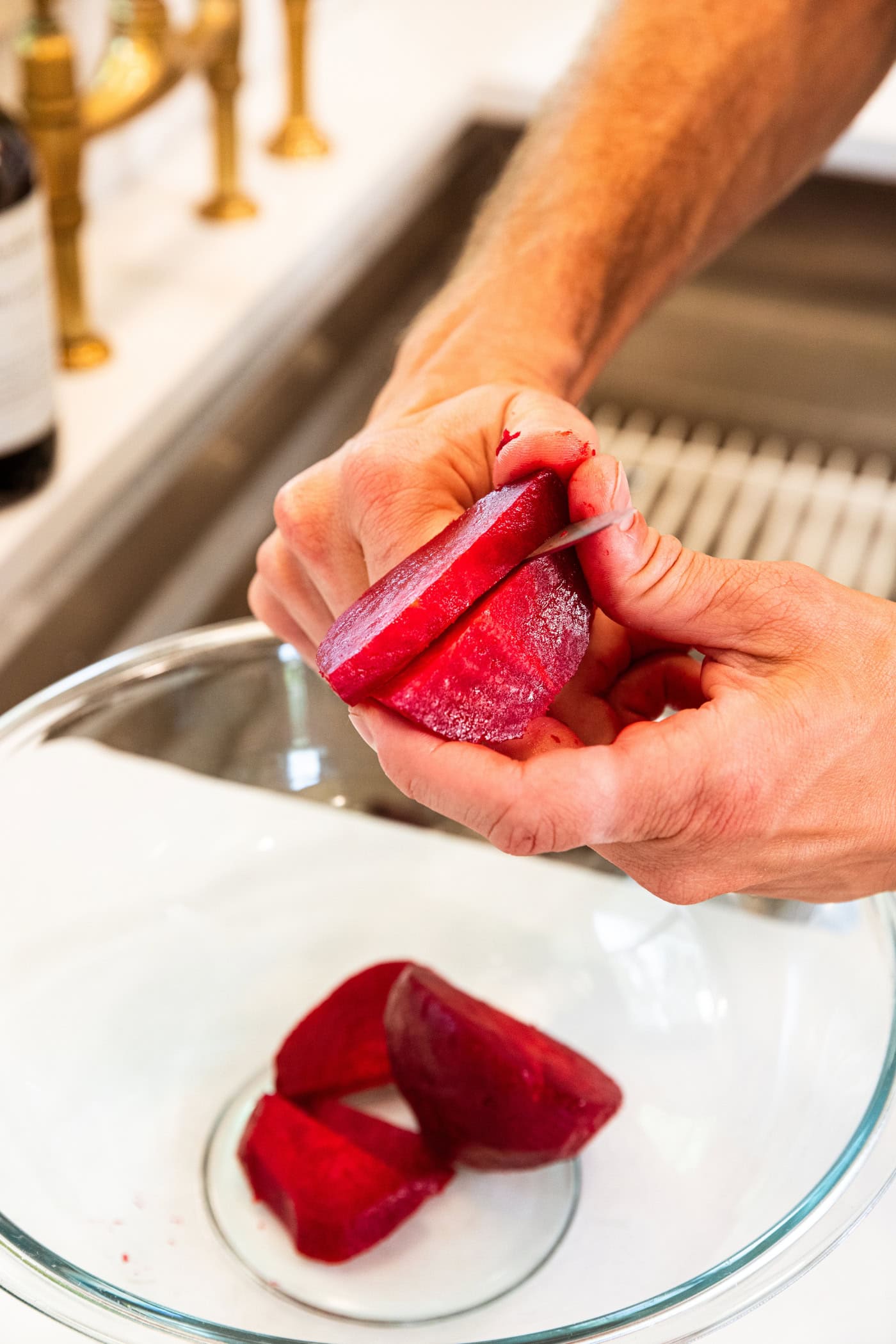 Hand holding cooked beet slicing it into slices in a glass bowl.