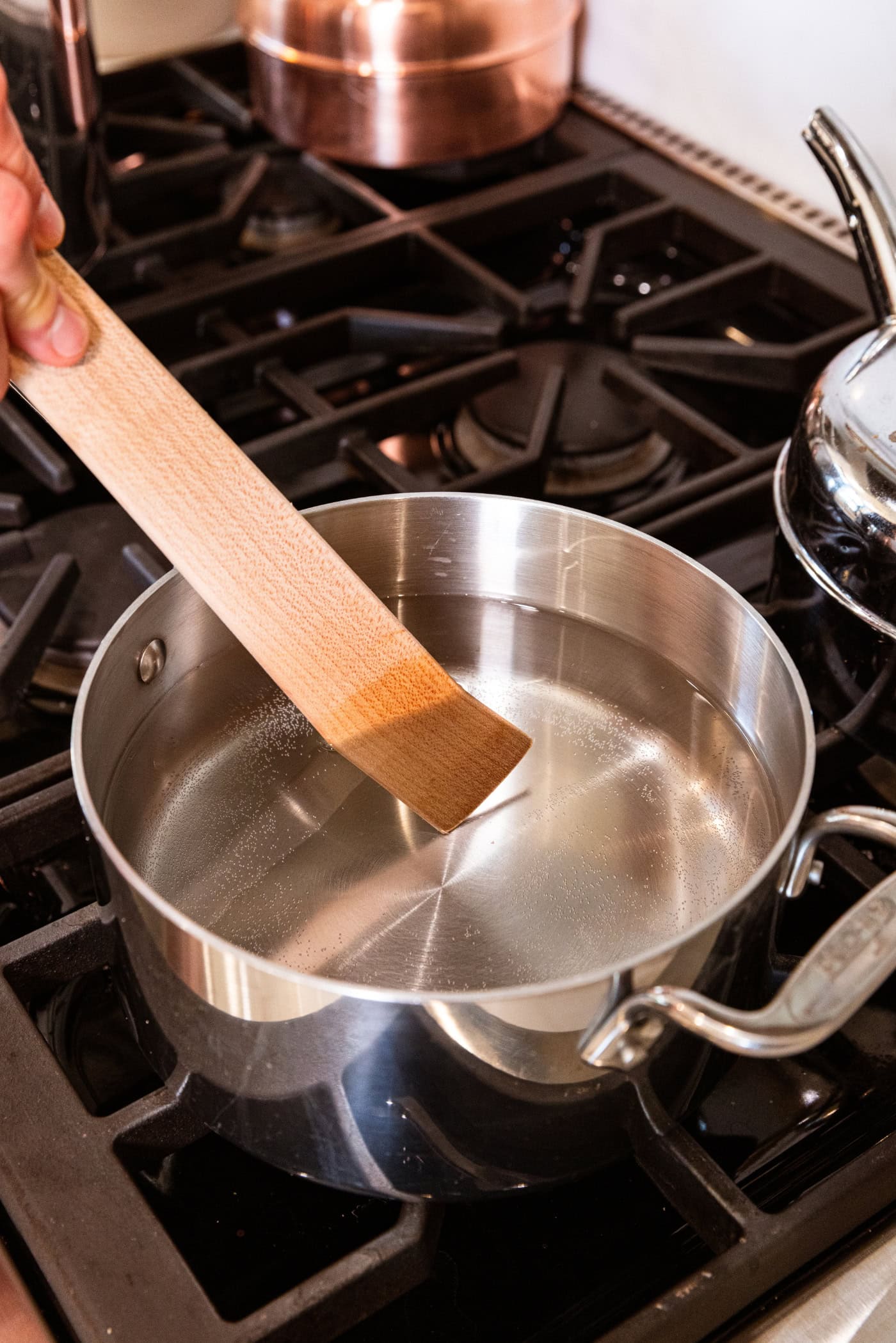 Wooden spatula stirring dissolved salt into vinegar mixture for a brine.