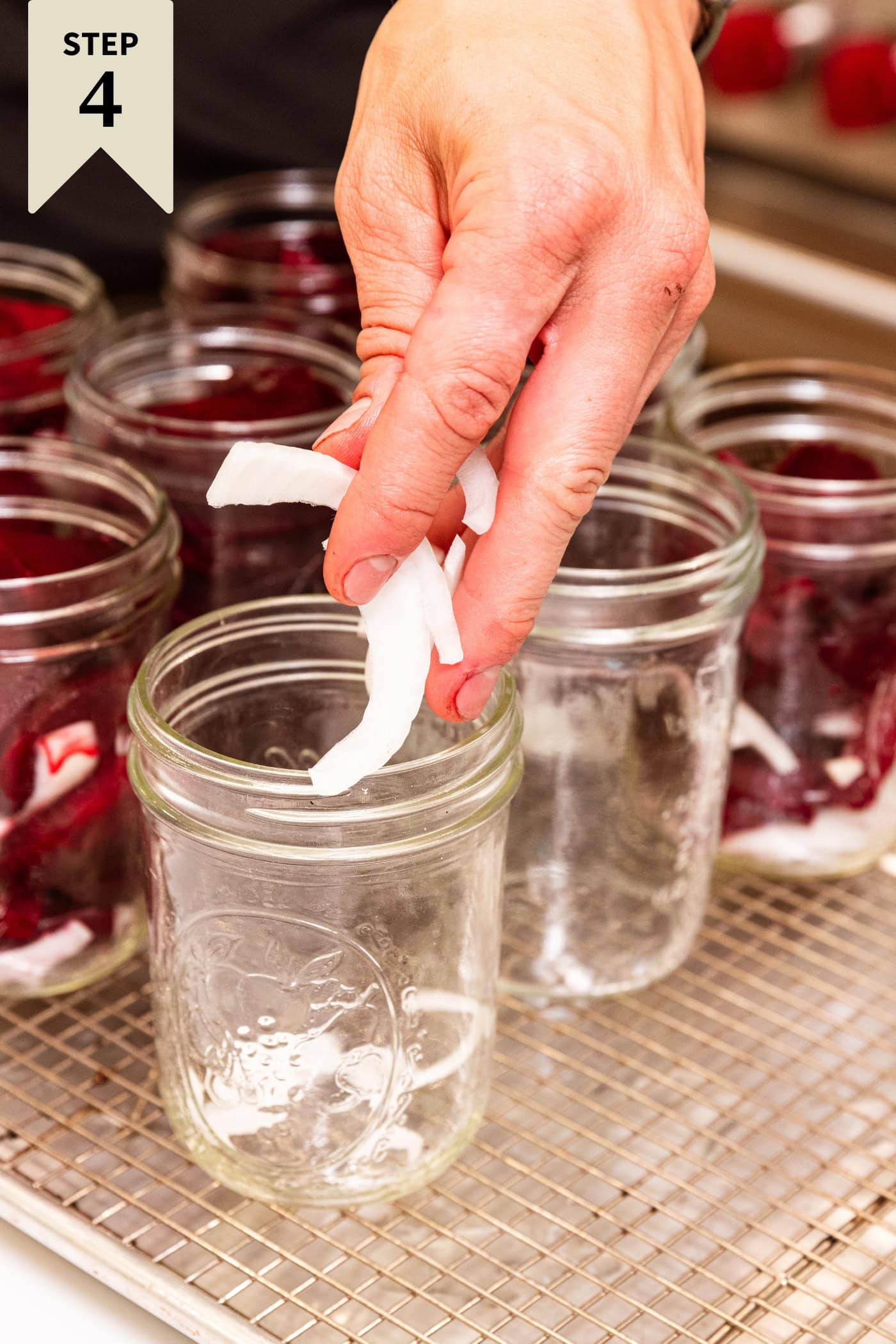 Hand holding slices of onion dropping them into the bottom of a glass jar for pickled beets.