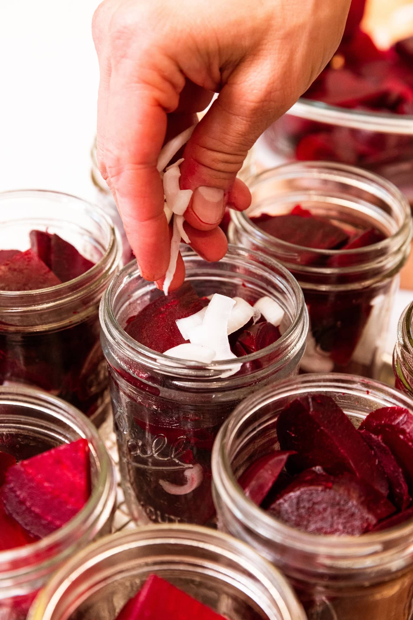 Hand placing slices of onion on top of beets in a canning jar for beets.