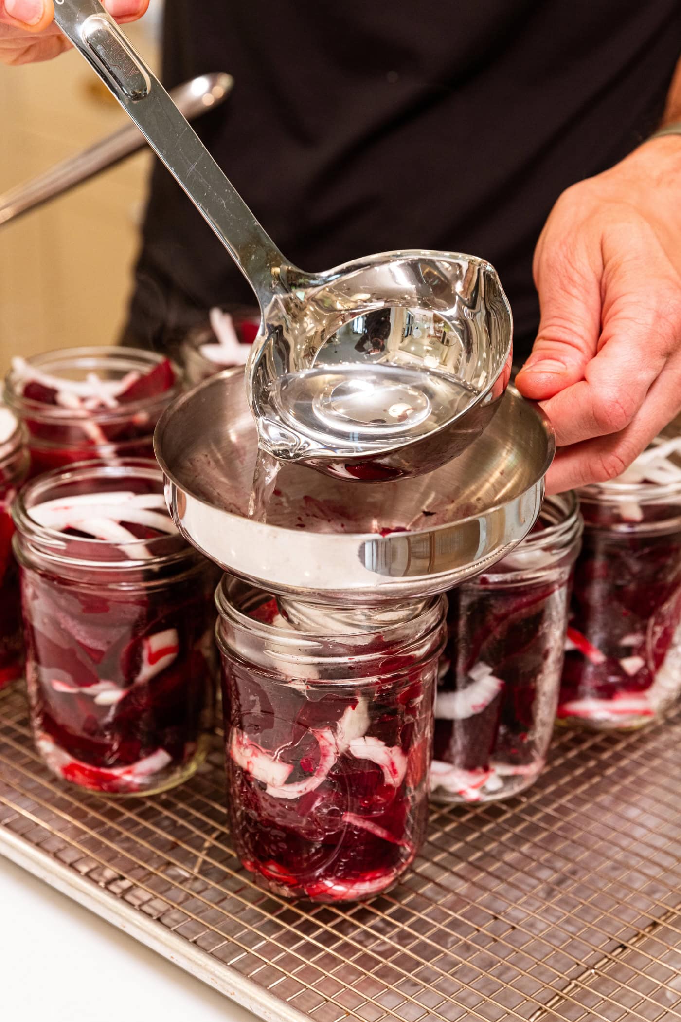 Ladle pouring vinegar brine on top of beet and onion mixture using a funnel.