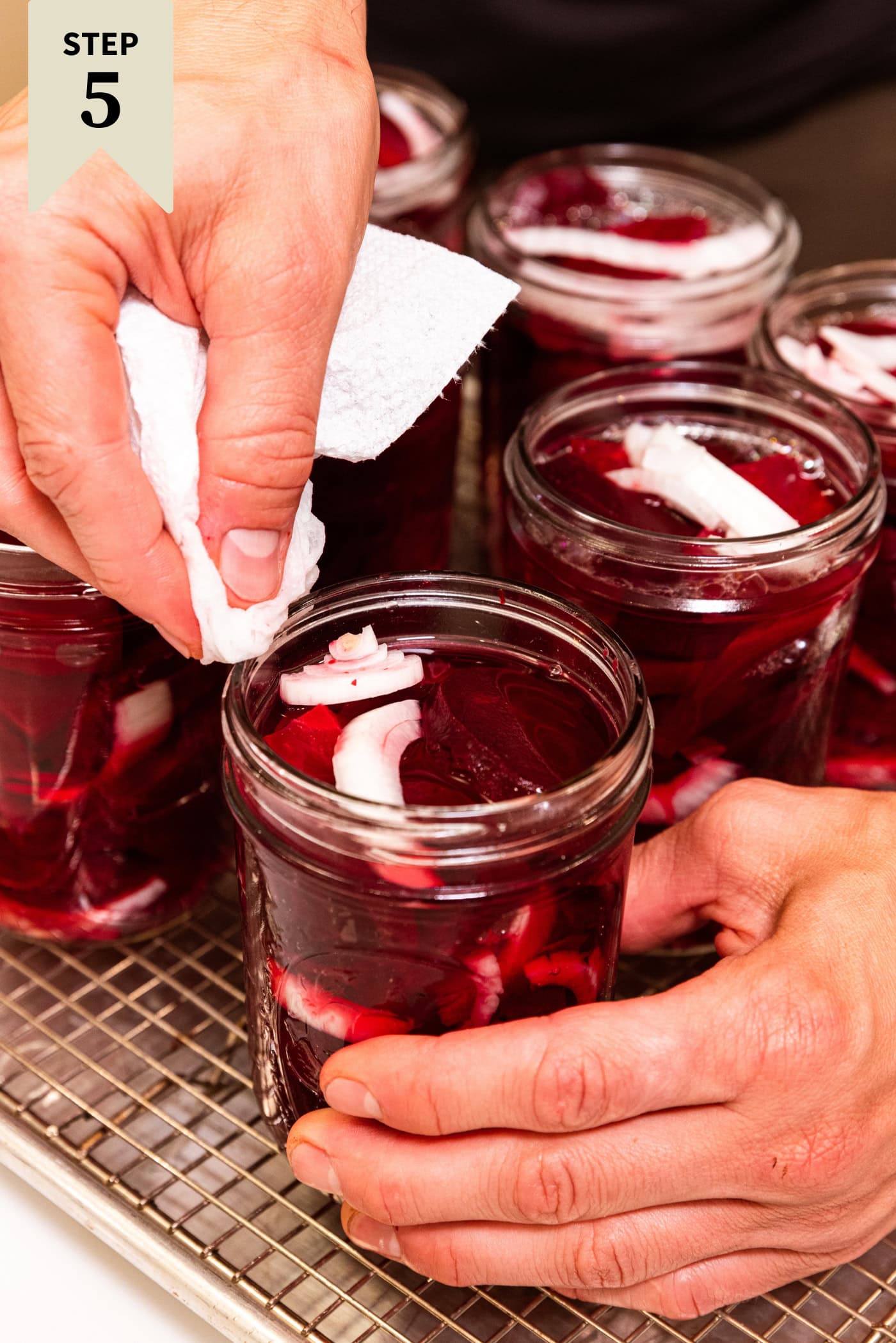 Hand wiping rim of a canning jar filled with beets with clean water from a paper towel.