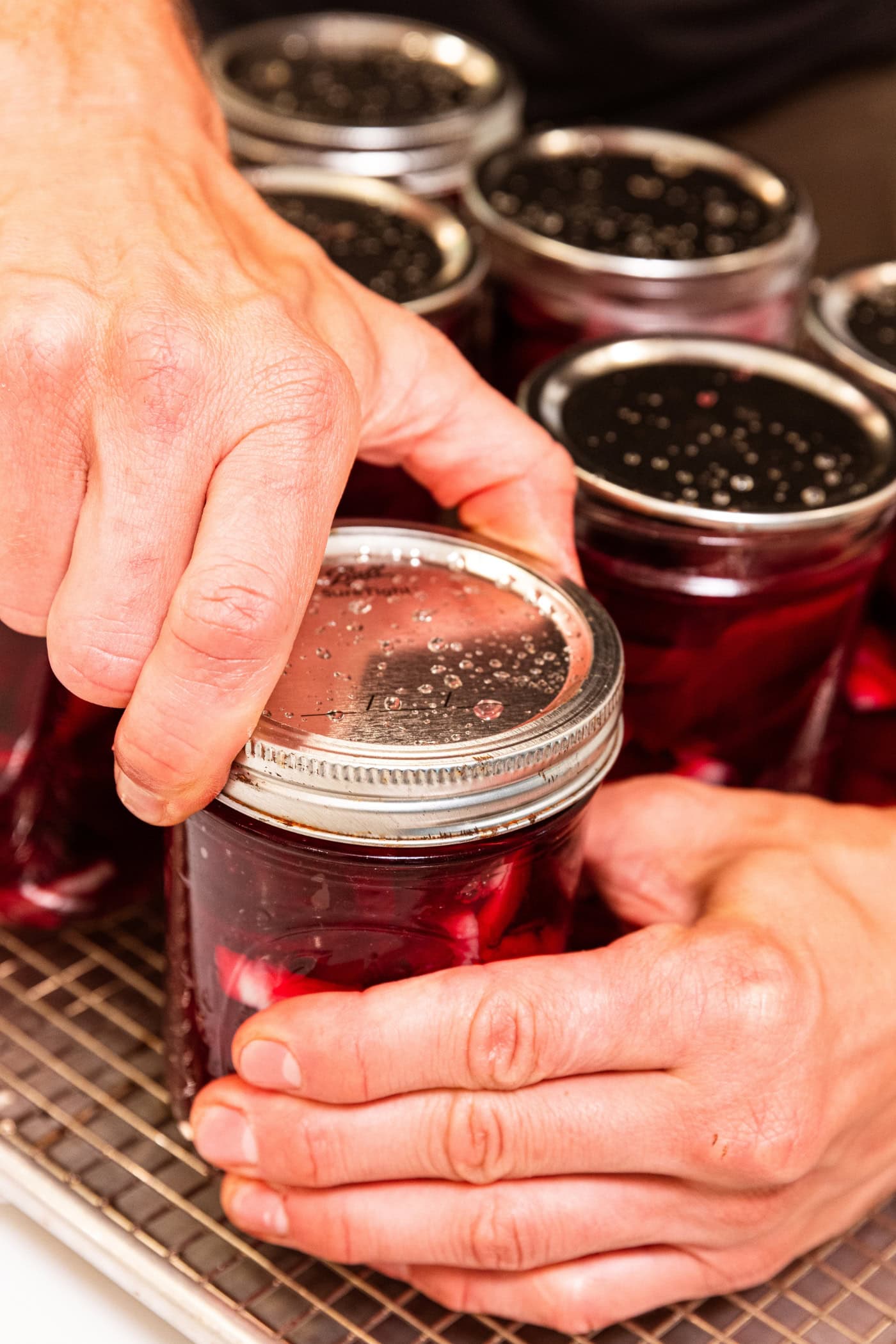 Hand putting lid and ring on canning jar filled with beets.