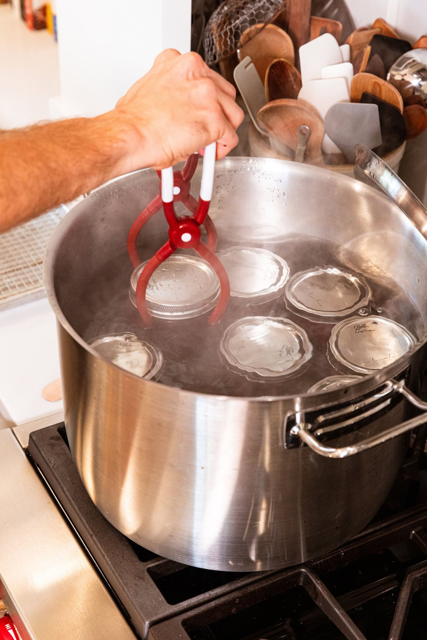 Hand placing canning jar into large canner on the stovetop with lots of other jars inside as well.