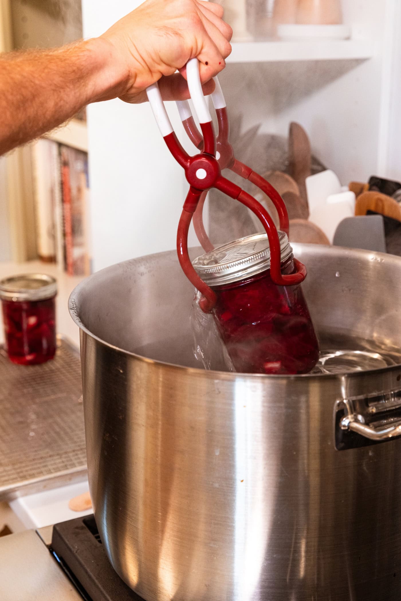 Hand using a jar lifter to lift a canning jar filled with beets out of the canner on the stovetop.