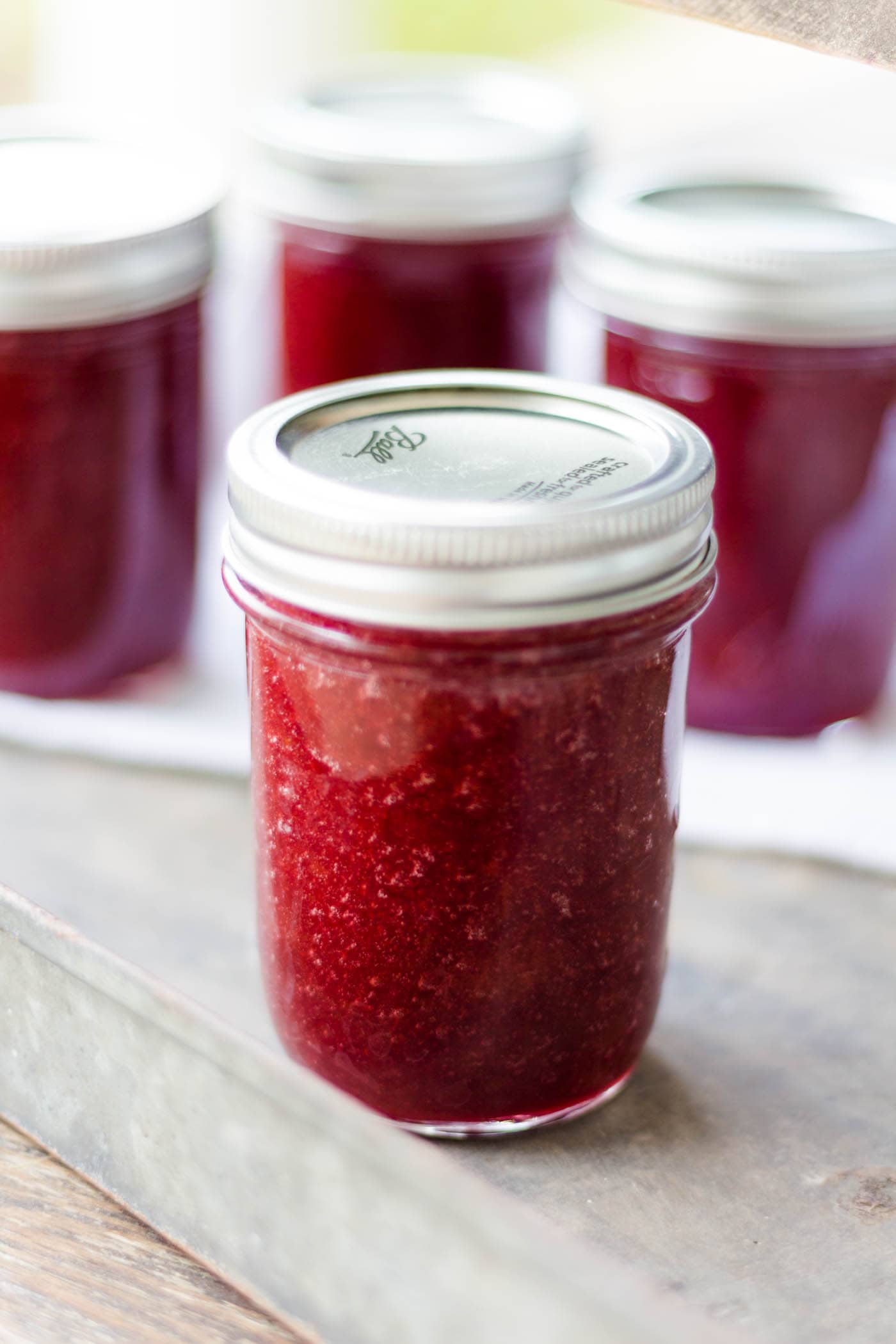 Jar of rhubarb butter on a silver metal tray with extra jars of rhubarb butter in background with white towel underneath